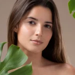 Young woman with clear glowing skin posing beside tropical leaves