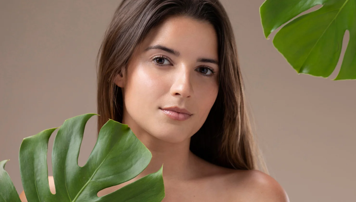 Young woman with clear glowing skin posing beside tropical leaves